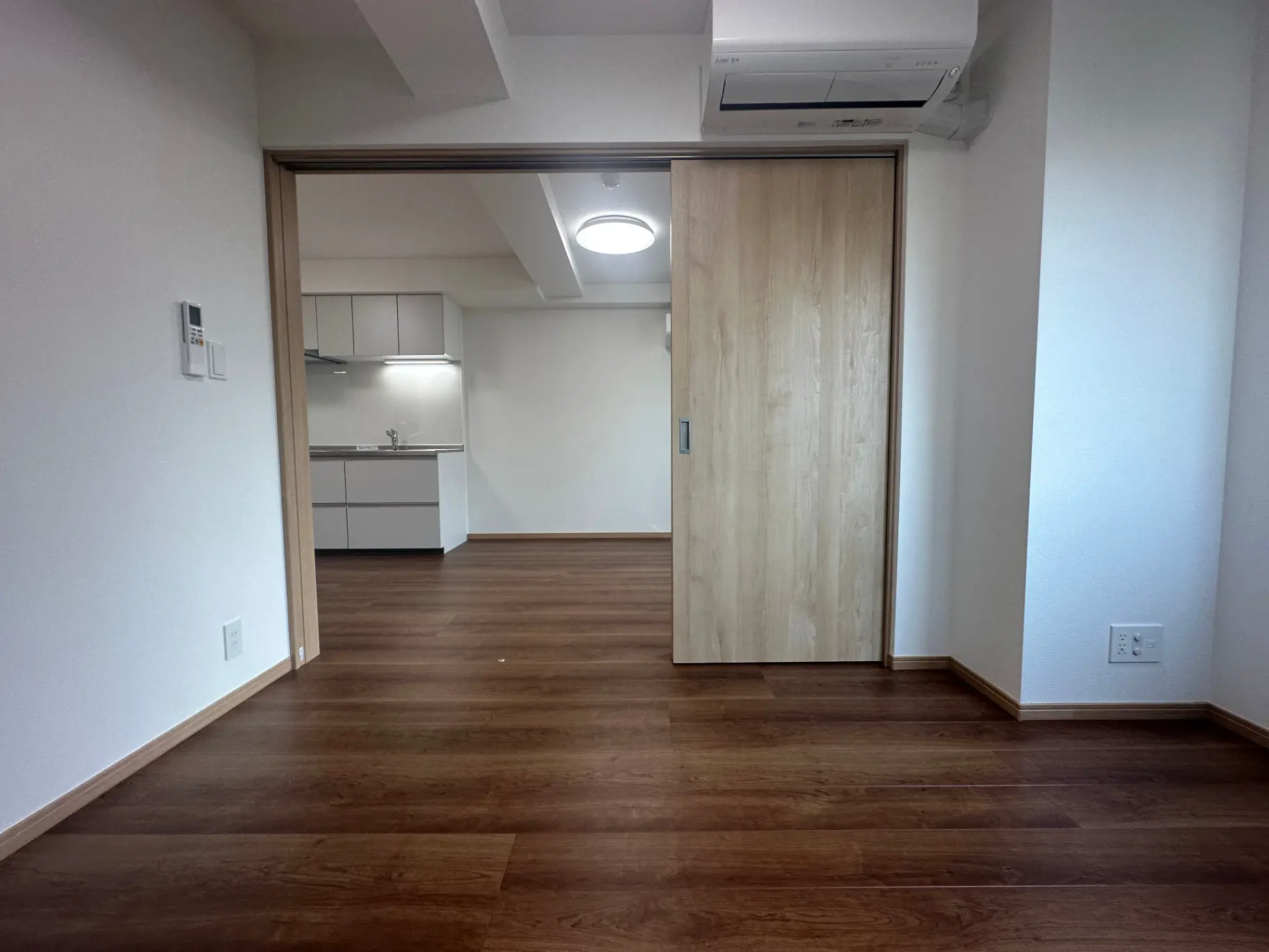 シンプルなデザインの空の部屋とキッチン、木製フロアと白い壁、エアコン付きのモダンなインテリア