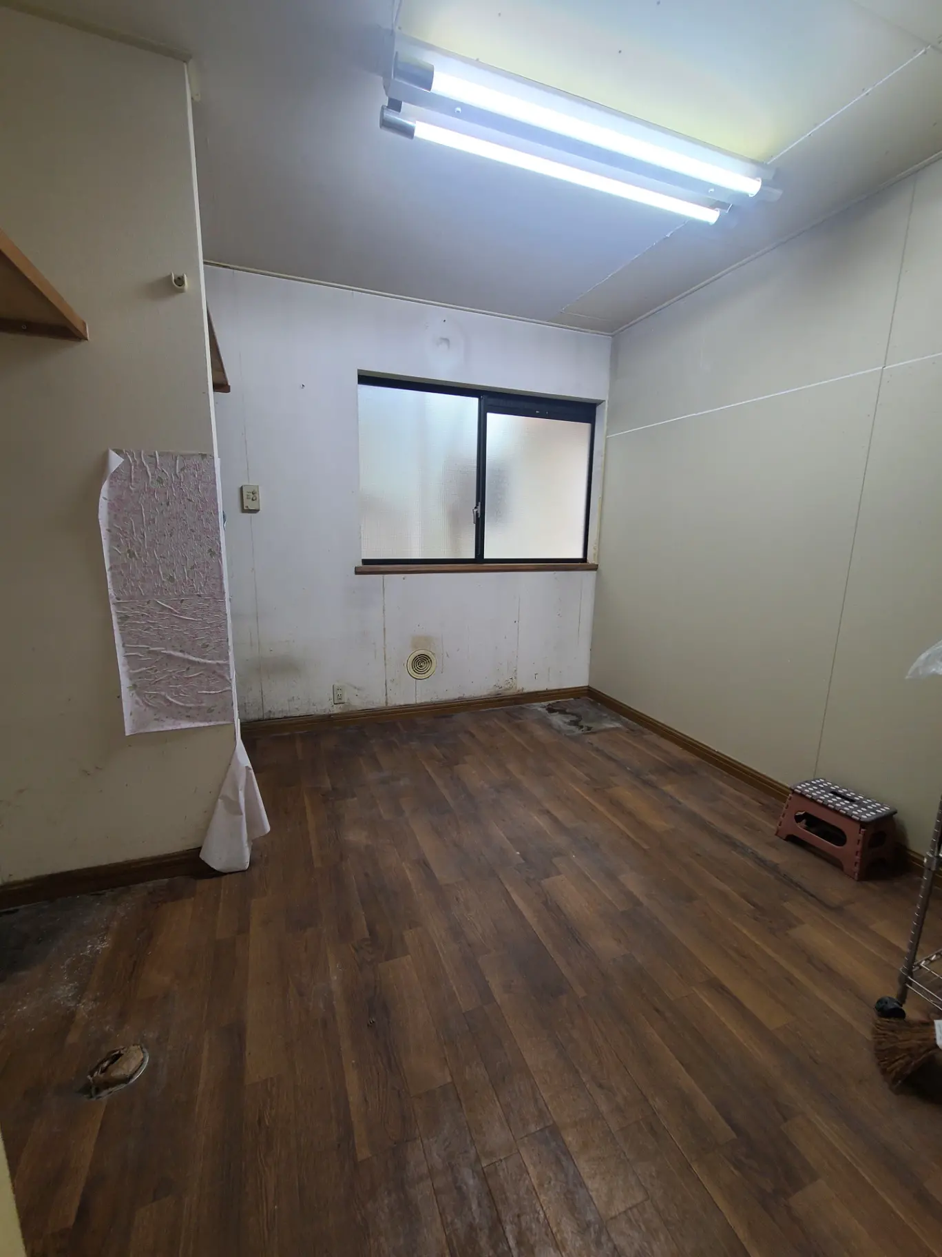 改装前の空き部屋、木製フロアに蛍光灯、壁に汚れあり