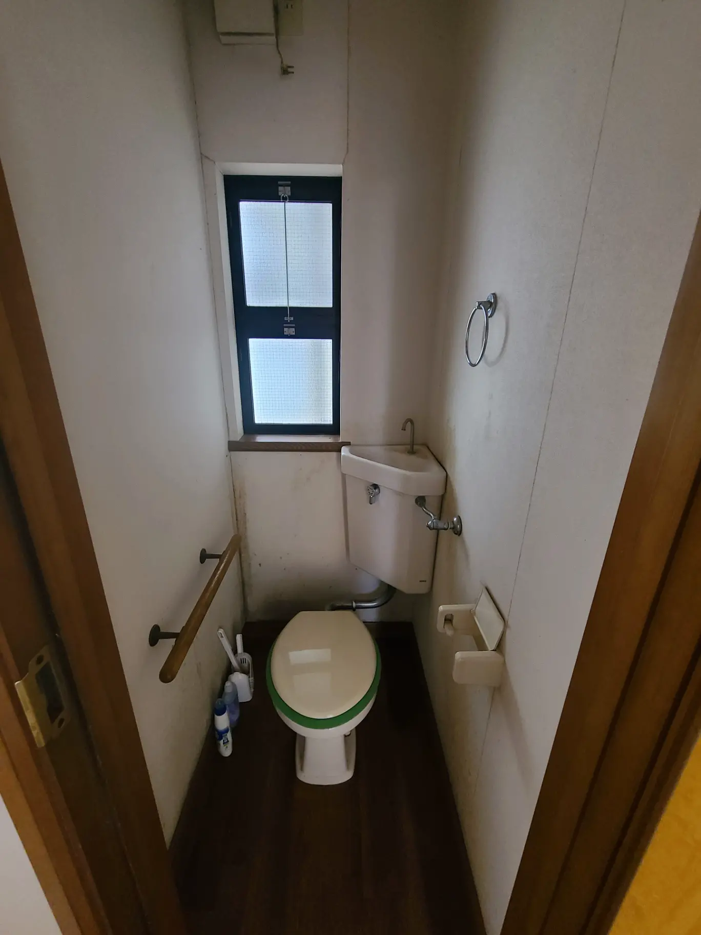 狭めのトイレルーム、白い壁、木目調の床、小窓と手すり付きのインテリア