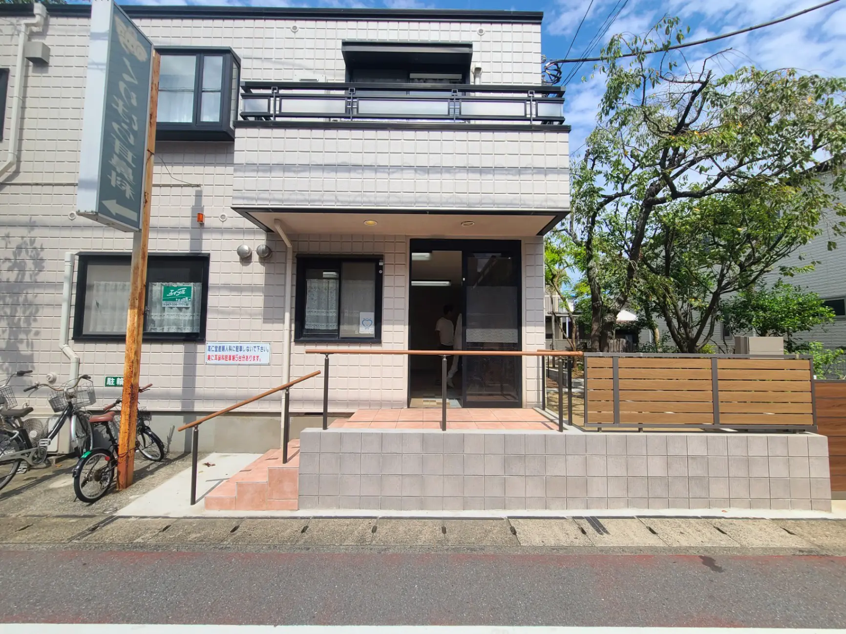 都会的な外観のカフェ、木製のフェンスと入り口の階段、自転車置き場あり