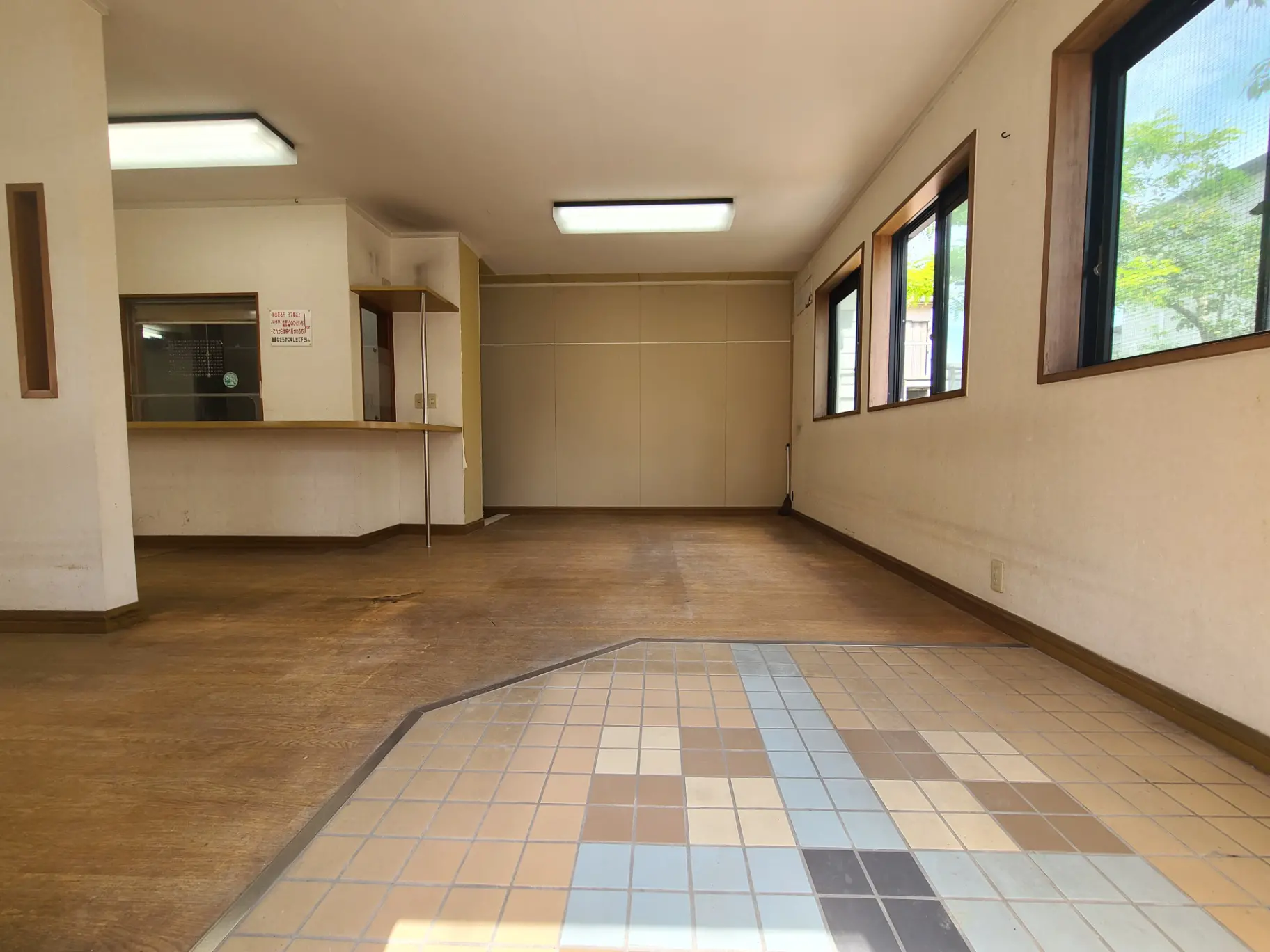 明るい窓と木製フロアの広々とした空き部屋、チェック柄タイルのエントランスエリア