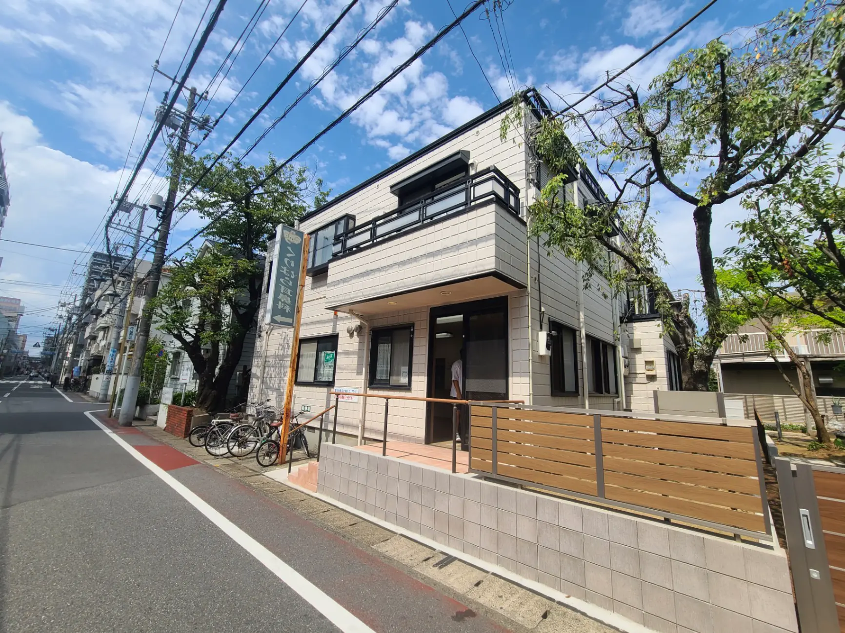 都市の通りに面したモダンな外観の建物、晴れた日の青空、通りに沿った樹木と電線