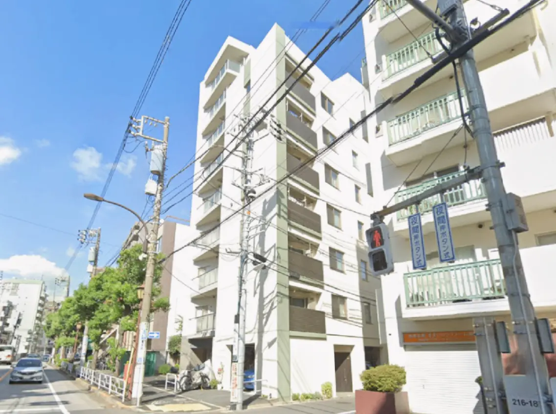 - 都市の一角にある白い外観の住宅ビル、青空と電柱が広がる街並みの風景