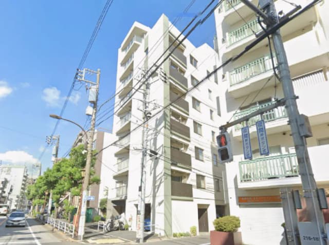 - 都市の一角にある白い外観の住宅ビル、青空と電柱が広がる街並みの風景