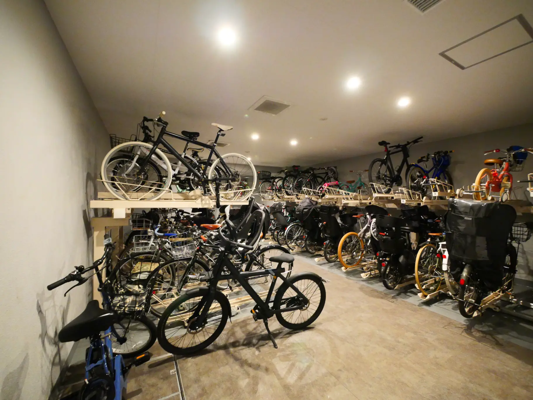室内駐輪場に多様な自転車が並ぶ光景、壁掛けラックと床置きの配置