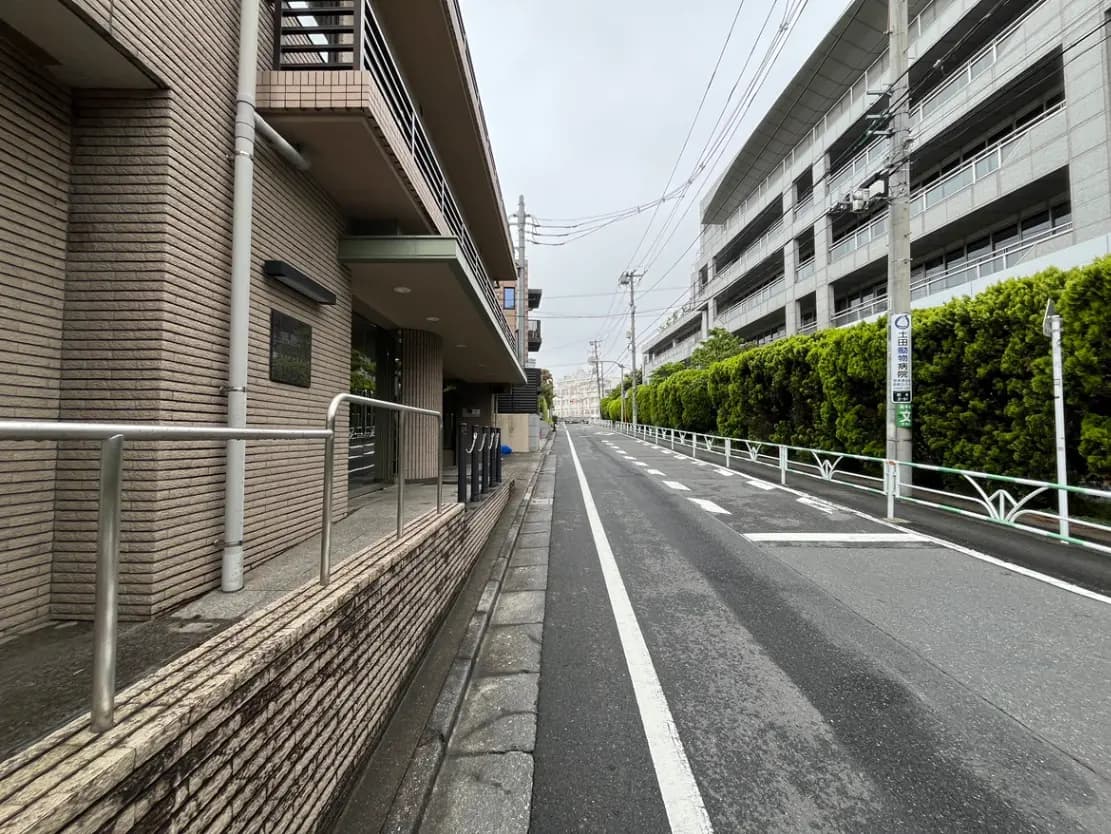 - モダンな建物の外観、整備された歩道と道路、緑豊かな生垣が並ぶ静かな街並みの景観