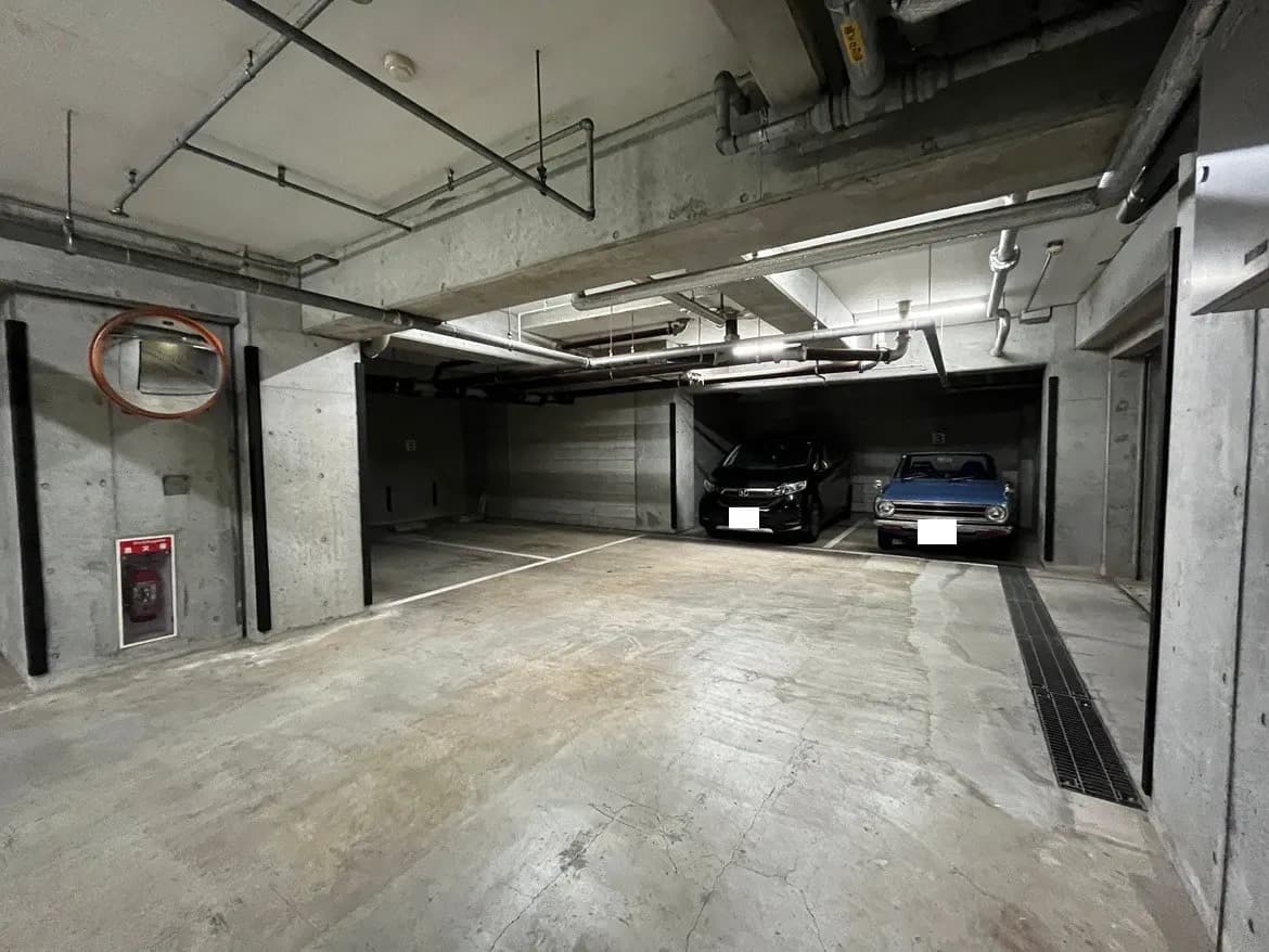 - コンクリート製の駐車場、２台の車が停まっている広々としたスペース、上部に配管が見える清潔感のあるデザイン