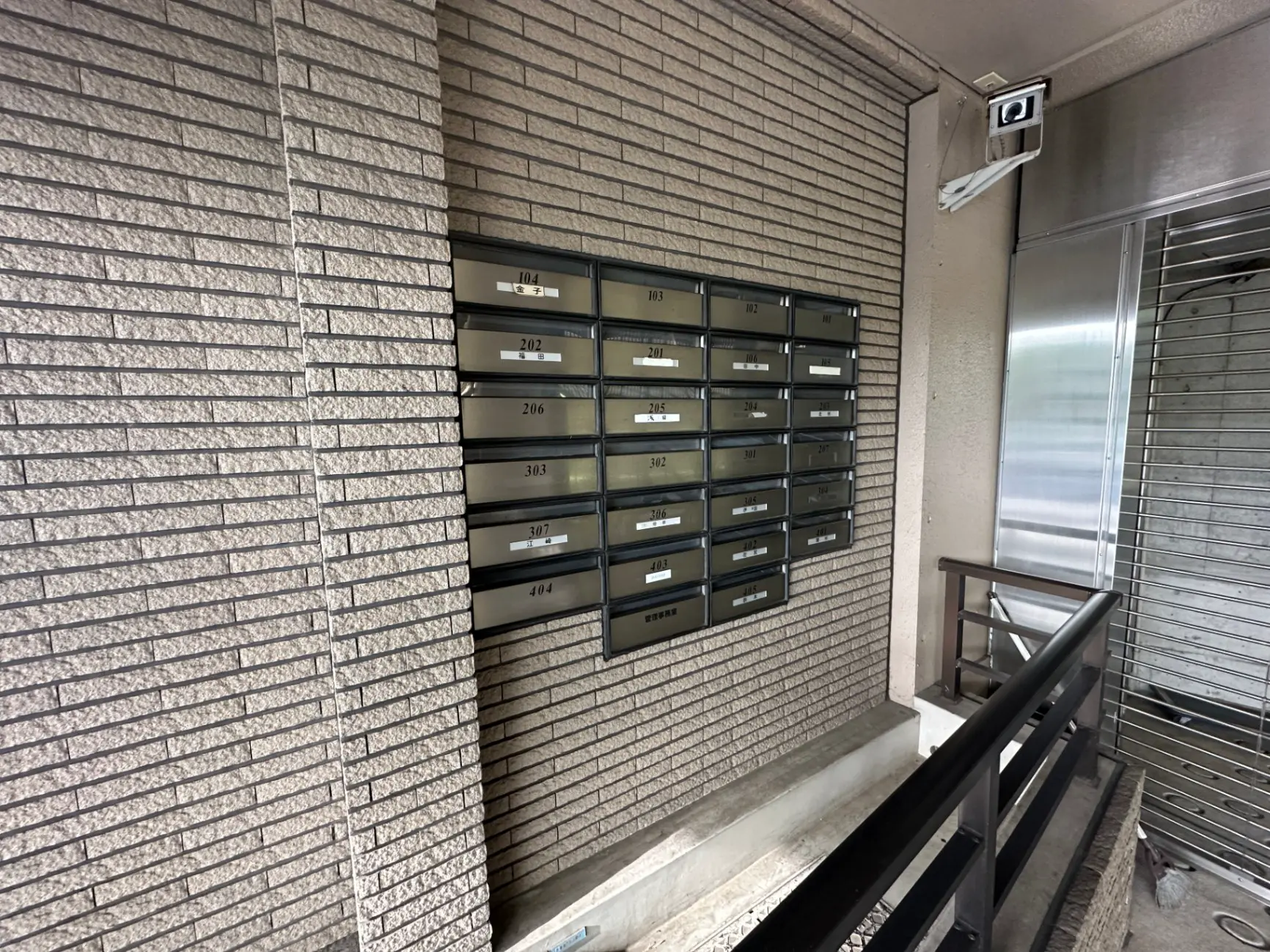 マンションのエントランスにある郵便受け、セキュリティカメラ付き、階段と照明のある共有スペース