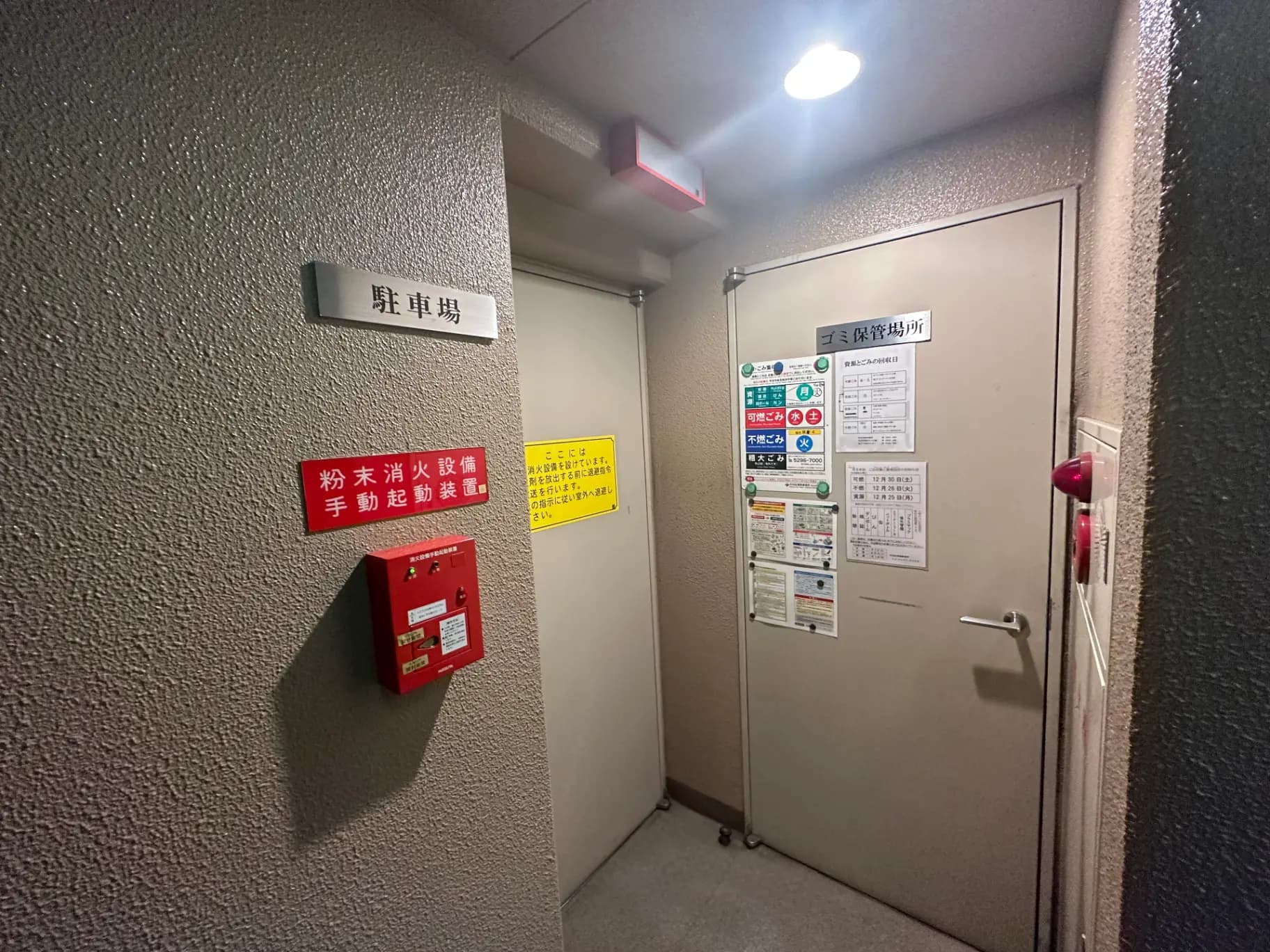 非常用インターホンと消火器が設置されたビルの避難口付近、多くの安全指示と規制の掲示物がある廊下