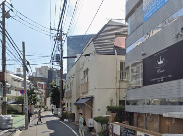 - 商業ビルと白い住宅が並ぶ街並み、道路沿いの電柱と電線が見える風景