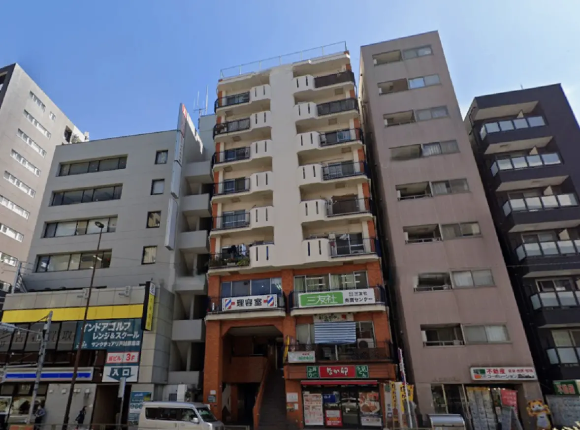 - 都市部にある複数階建てのアパートメントビル、店舗前に看板や自動販売機が設置されている様子