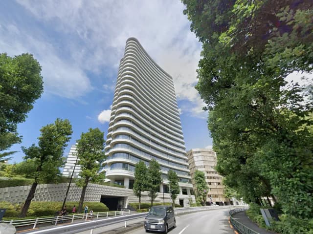 青空の下、曲線的なデザインのモダンなオフィスビル外観、街路樹と車が走る都市の風景