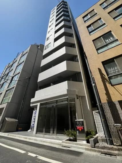 - モダンなデザインの高層マンション、白いタイル張りの外壁、開放的なエントランス、周囲の建物と明るい空の背景