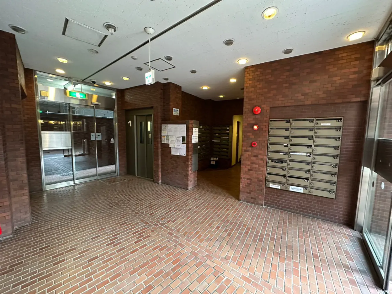 レンガ造りの壁と床が特徴的なマンションエントランスホール、自動ドアと郵便受けが設置されているキレイな共用スペース