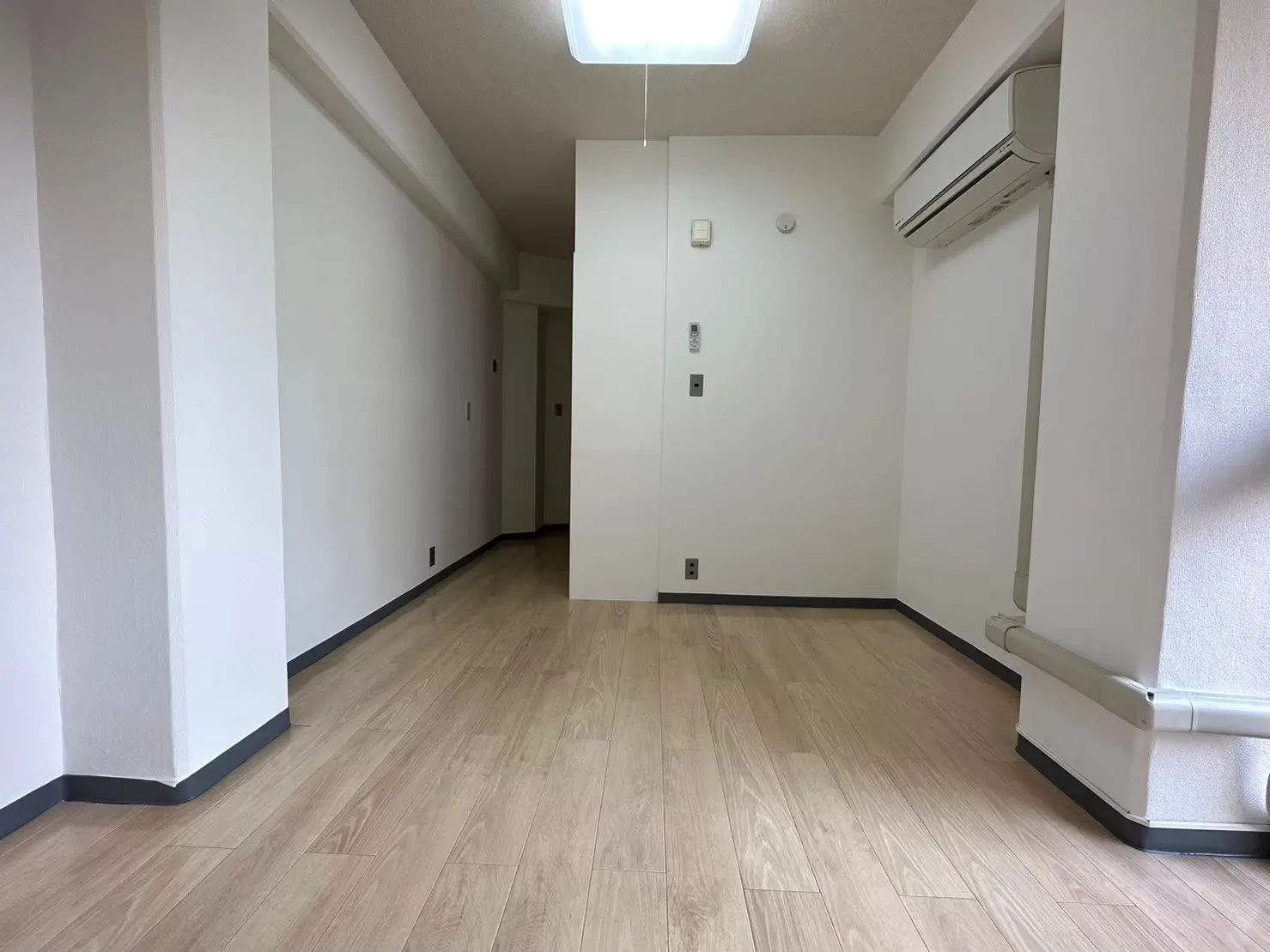 シンプルな内装の空の部屋、木目調のフローリング、白い壁、エアコン付き