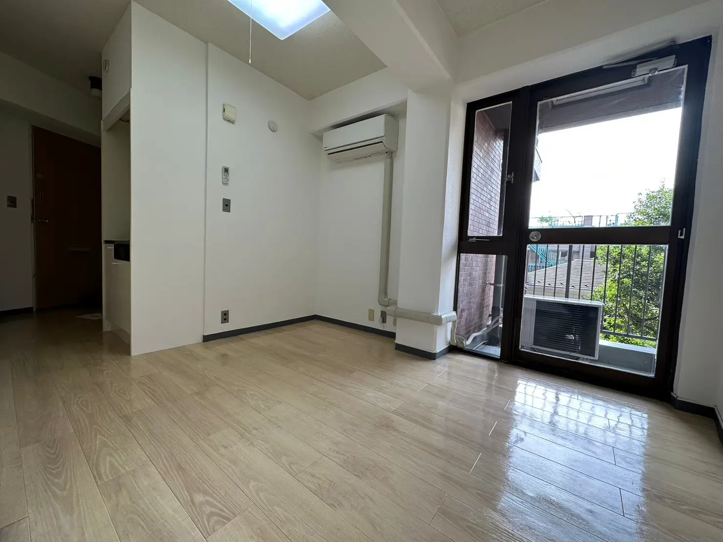 明るく広々とした空の部屋、木目調フローリング、白い壁、窓から自然光が差し込むインテリア