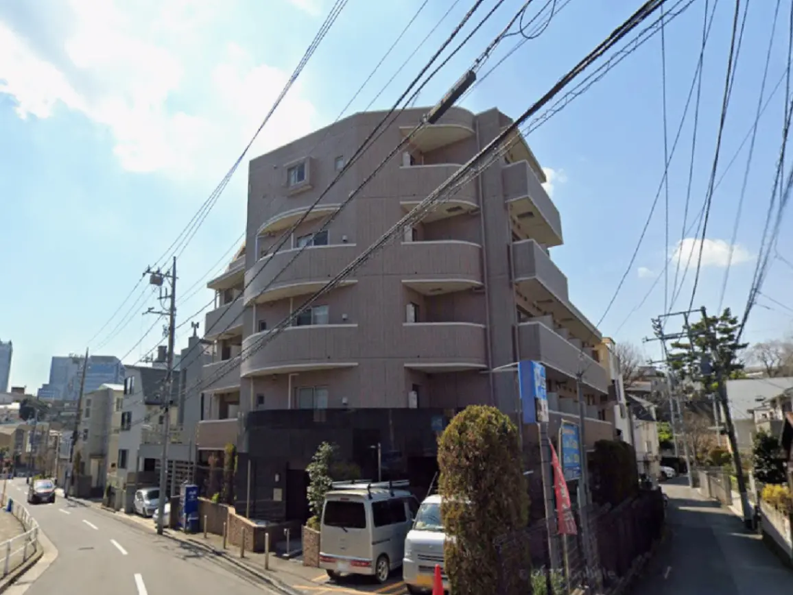 - 都市部に位置するモダンなアパートメントビルの外観、周囲には電柱と緑が配置された街並み