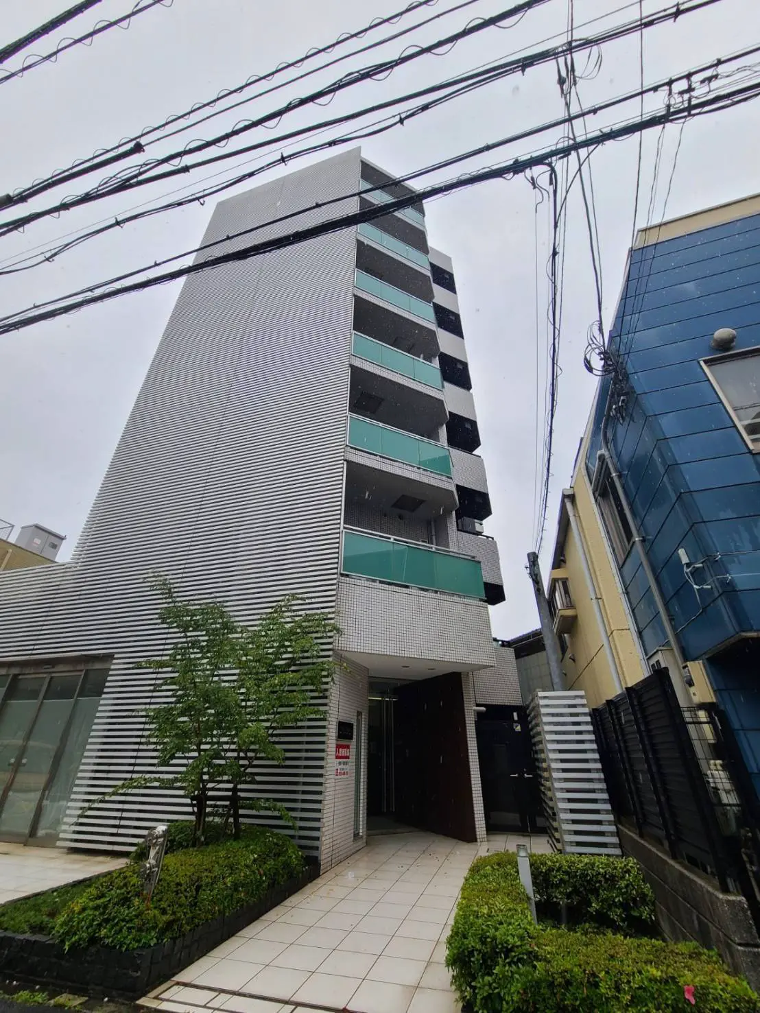 都会的なマンションの外観、ストライプ模様の壁面デザイン、前面に小さな庭園