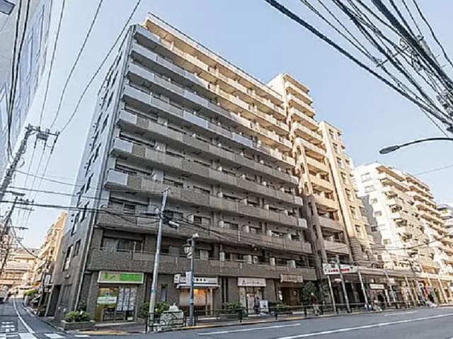 - 都市の商業エリアに位置する高層マンションの外観、周囲には店舗や飲食店が立ち並ぶ繁華街の様子