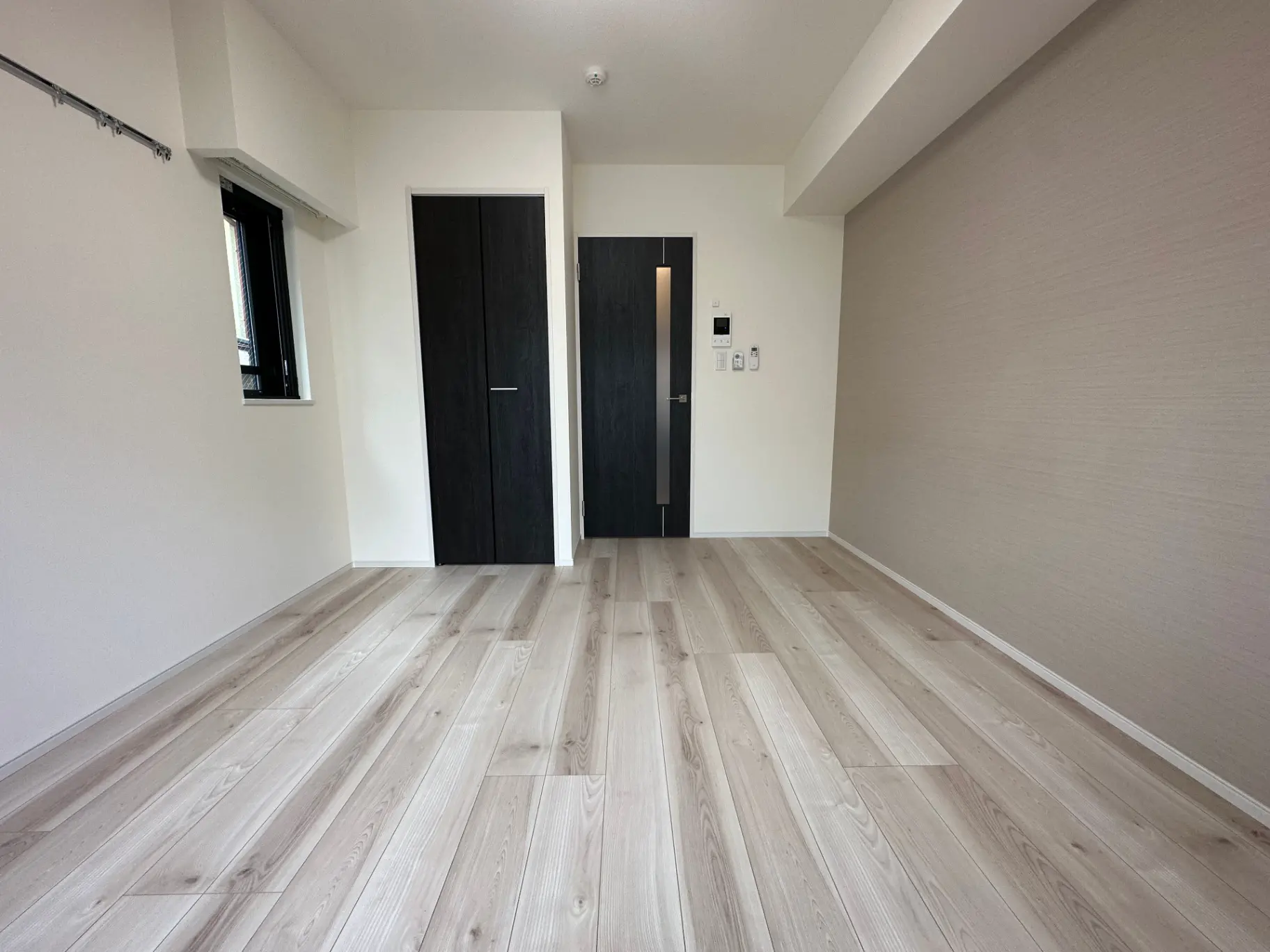 新築マンションの空の部屋、ライトウッドのフロア、白壁、入口ドアと小窓