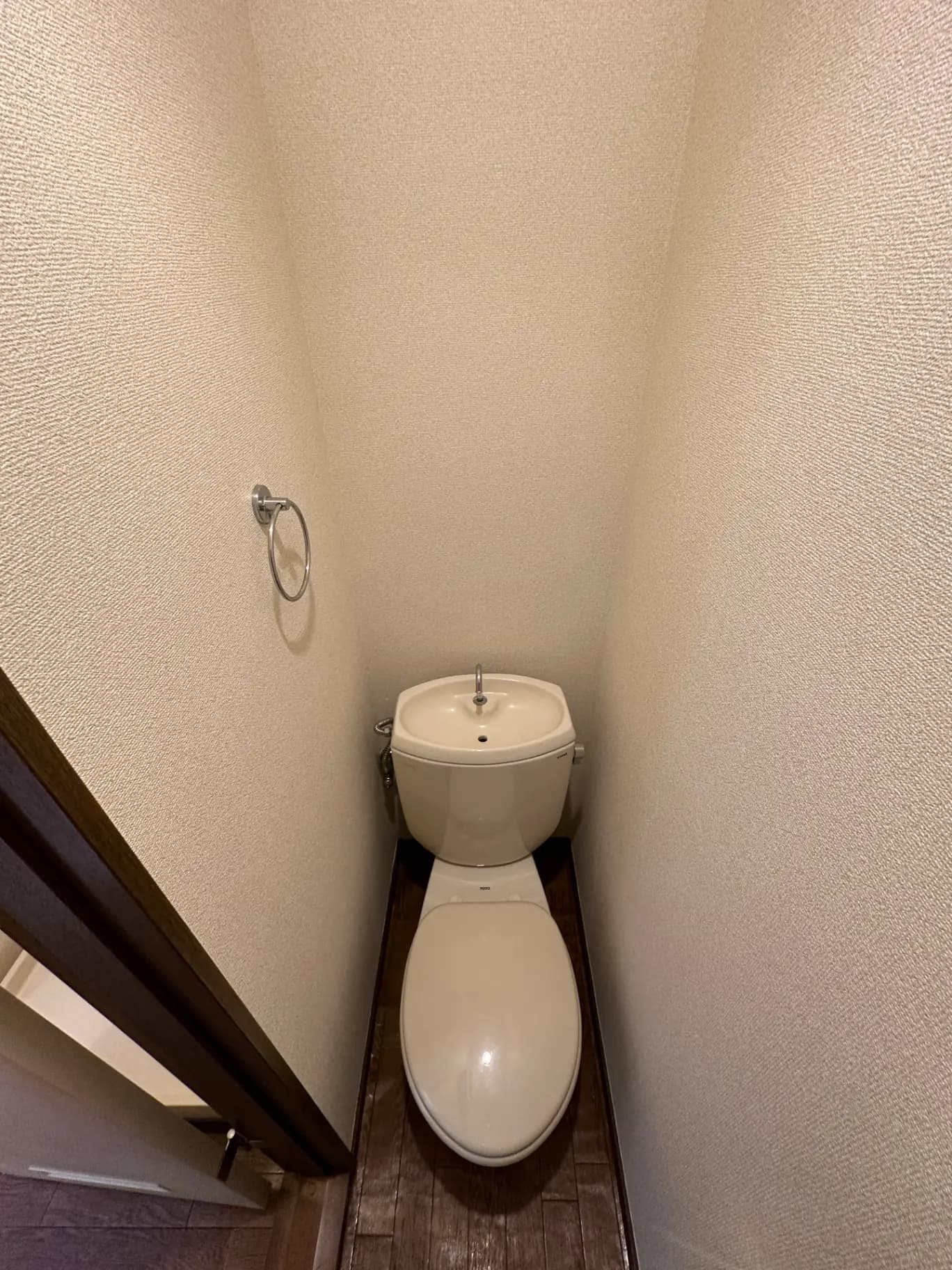 狭い空間に収められた洋式トイレ、木目調の床、壁にトイレットペーパーホルダー