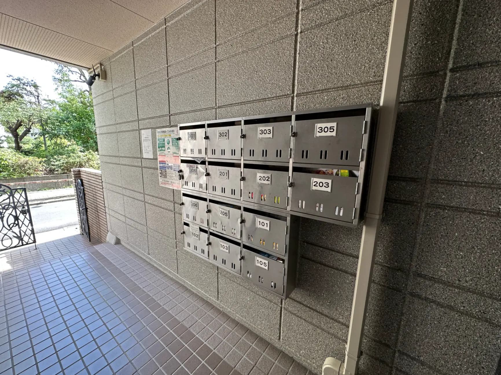 マンションのエントランスにある郵便受け、番号付きのメールボックス、自然光が差し込む共用スペース
