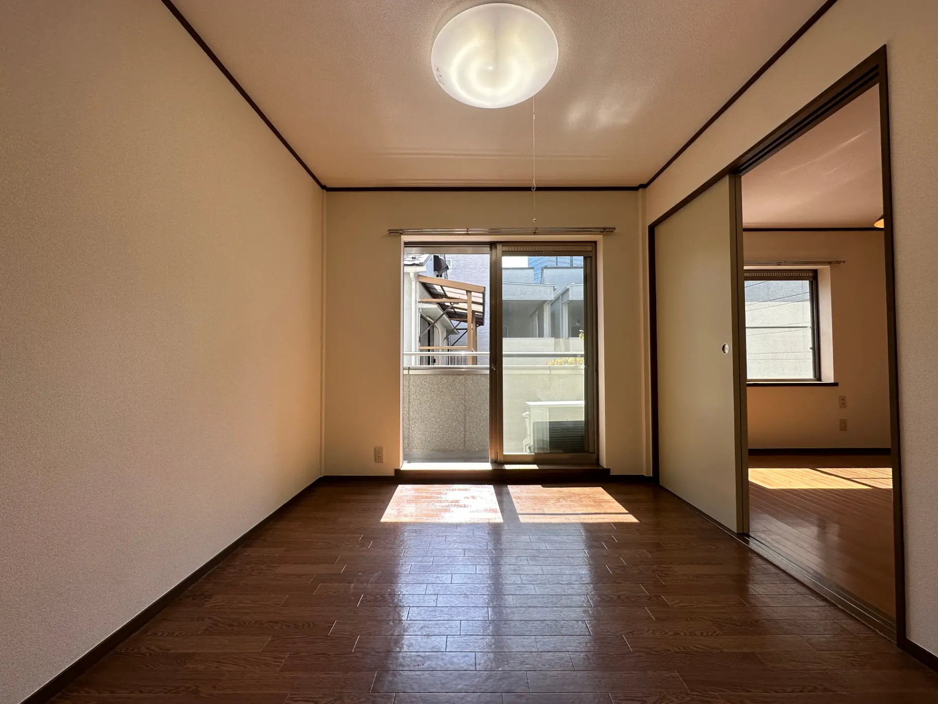 日当たりの良い明るい空間、茶色いフローリングが特徴的なリビングルーム、ガラスの引き戸とバルコニー付き