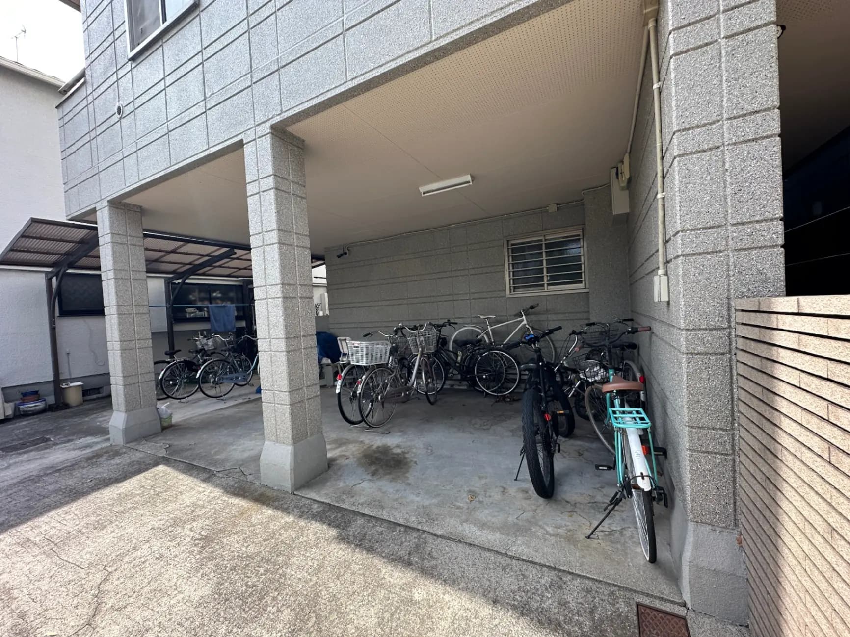 多くの自転車が置かれたアパートの駐輪場、グレーの壁と柱、コンクリートの床