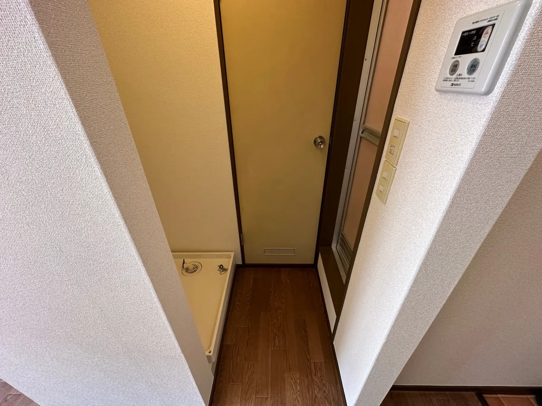 狭い廊下と部屋の入口、壁付けインターホンとスイッチ、木目調フローリング