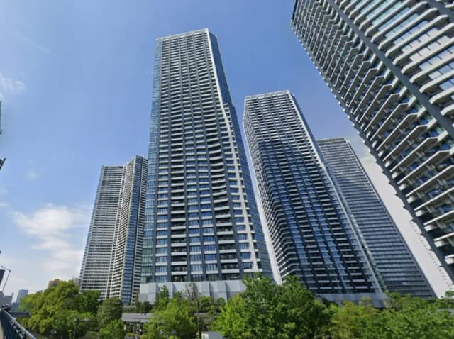 - 現代的な高層ビル群、青空の下にそびえ立ち、緑豊かな植栽が周囲を囲む都市景観
