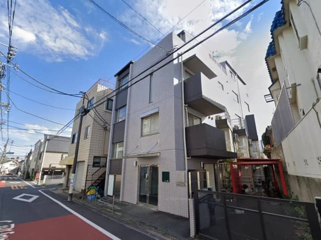 - 都市部に位置するモダンなアパートメントビルの外観、隣接した建物と青空が広がる風景