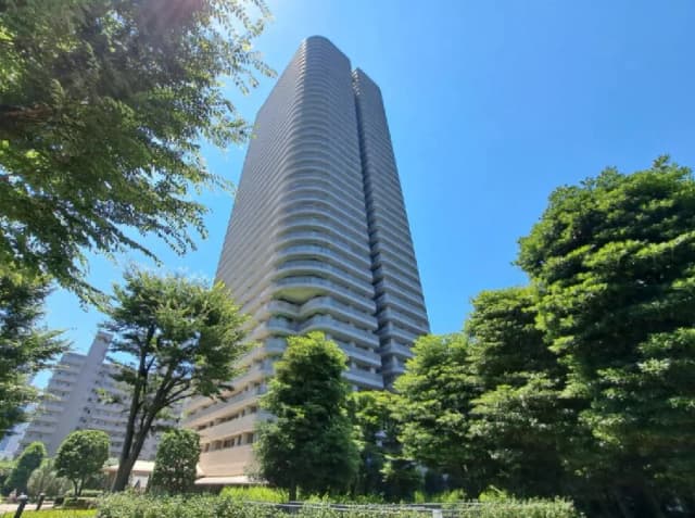 - 青空を背景にした高層マンション、周囲に緑豊かな樹木が並ぶ景観