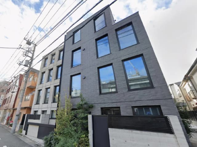 - 現代的なデザインのモダンなマンション、黒い外壁と大きな窓、周囲の緑と電線が見える街並み