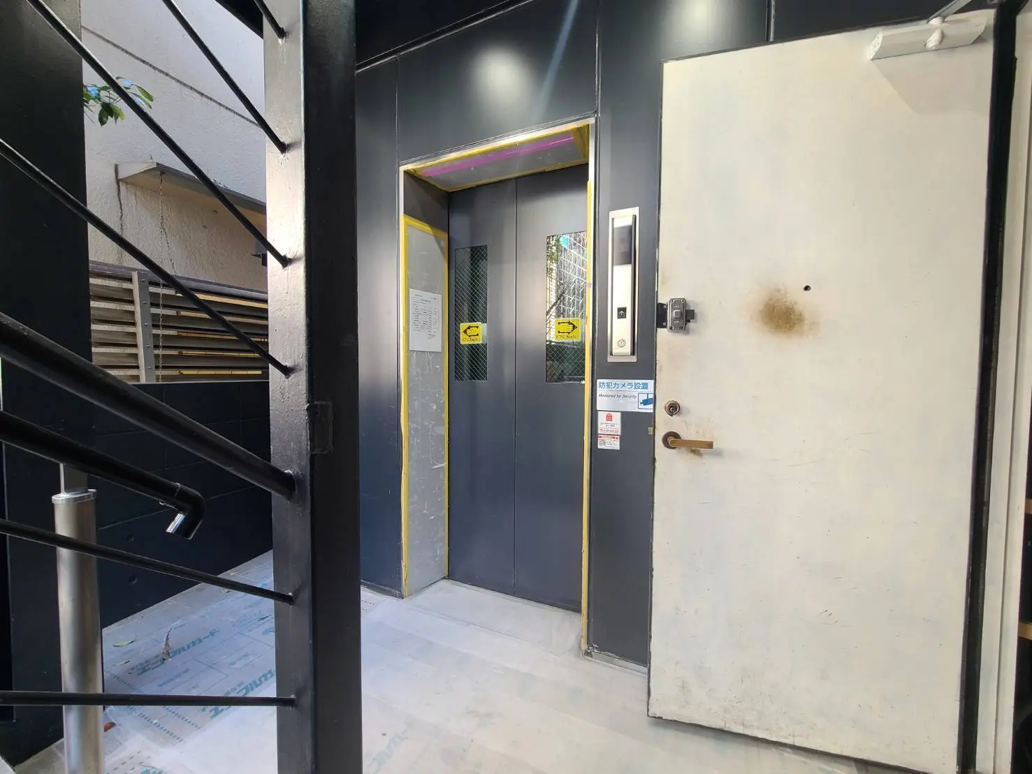 暗い色調のビルの入口、階段とエレベーター、セキュリティキーパッド付きの扉