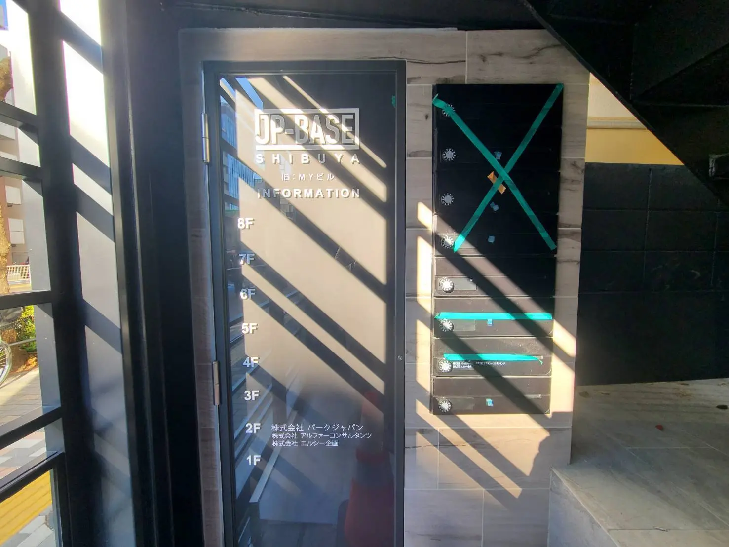 ビル入口の案内看板、透明デザインの階層表示と陽光が差し込むモダンなエントランス