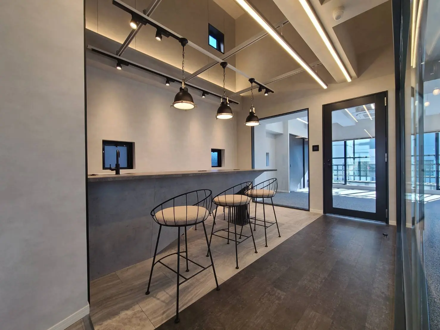 モダンなオフィスの共有スペース、スタイリッシュな照明とバーカウンター付きキッチン、床から天井までの窓