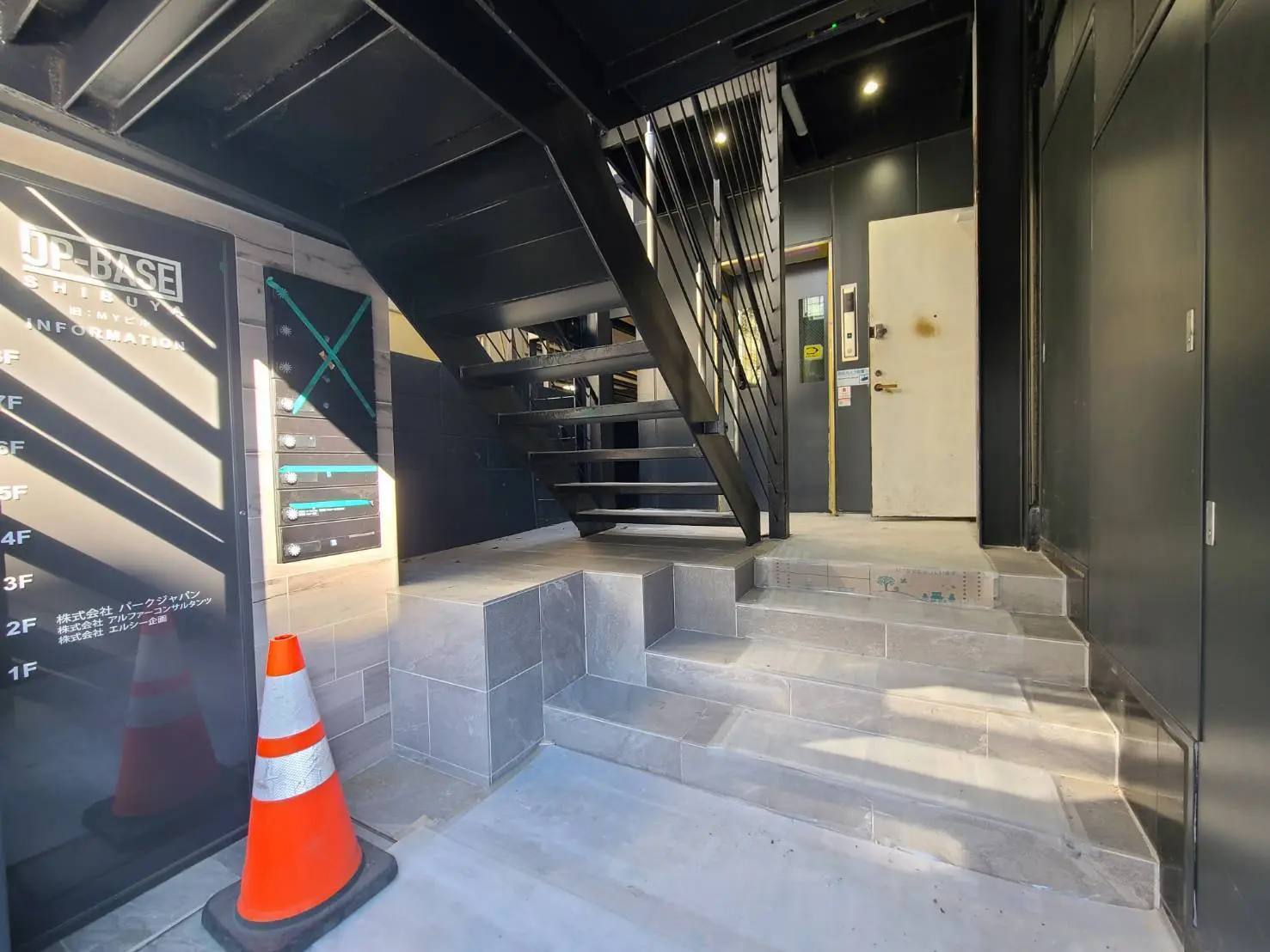 黒い金属製の階段とグレーのタイル張りのエントランス、案内サイン付きビルの内部