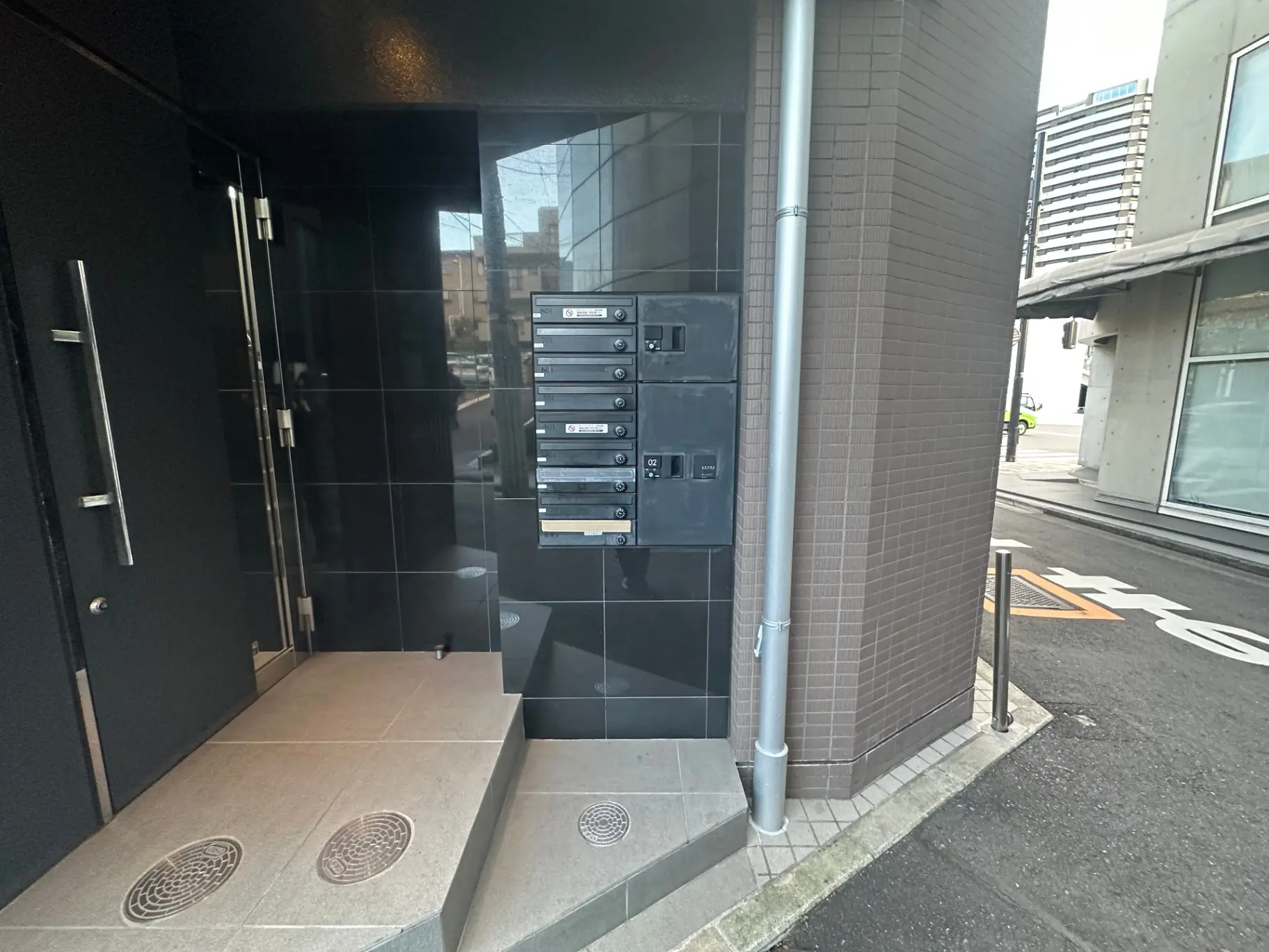 都市のマンション入り口、黒い壁とポスト、タイルの敷地