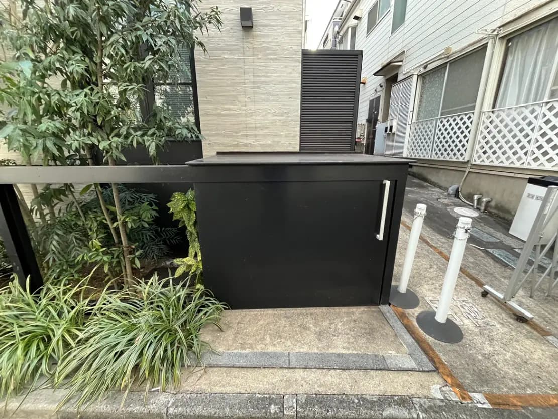 建物のエントランス付近に配置されたゴミ箱と緑豊かな植栽、都会的な外観デザイン