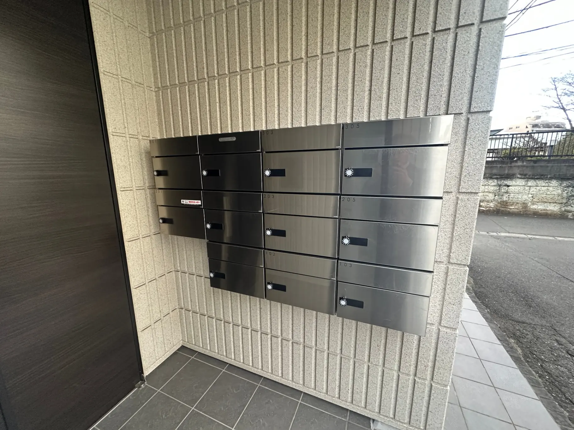 建物のエントランスにあるモダンなデザインの郵便受け、石造りの壁とタイルフロア