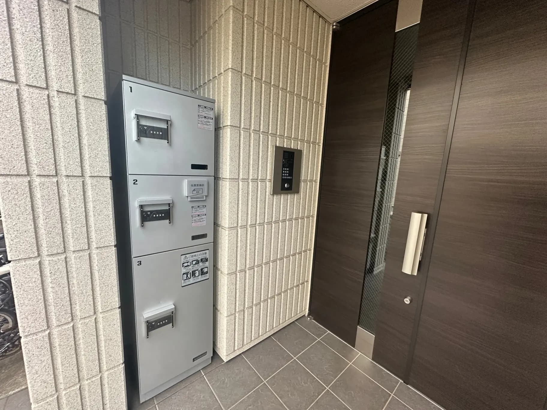 モダンなマンションの宅配ボックスとダークブラウンの入口ドア、タイルの壁と床