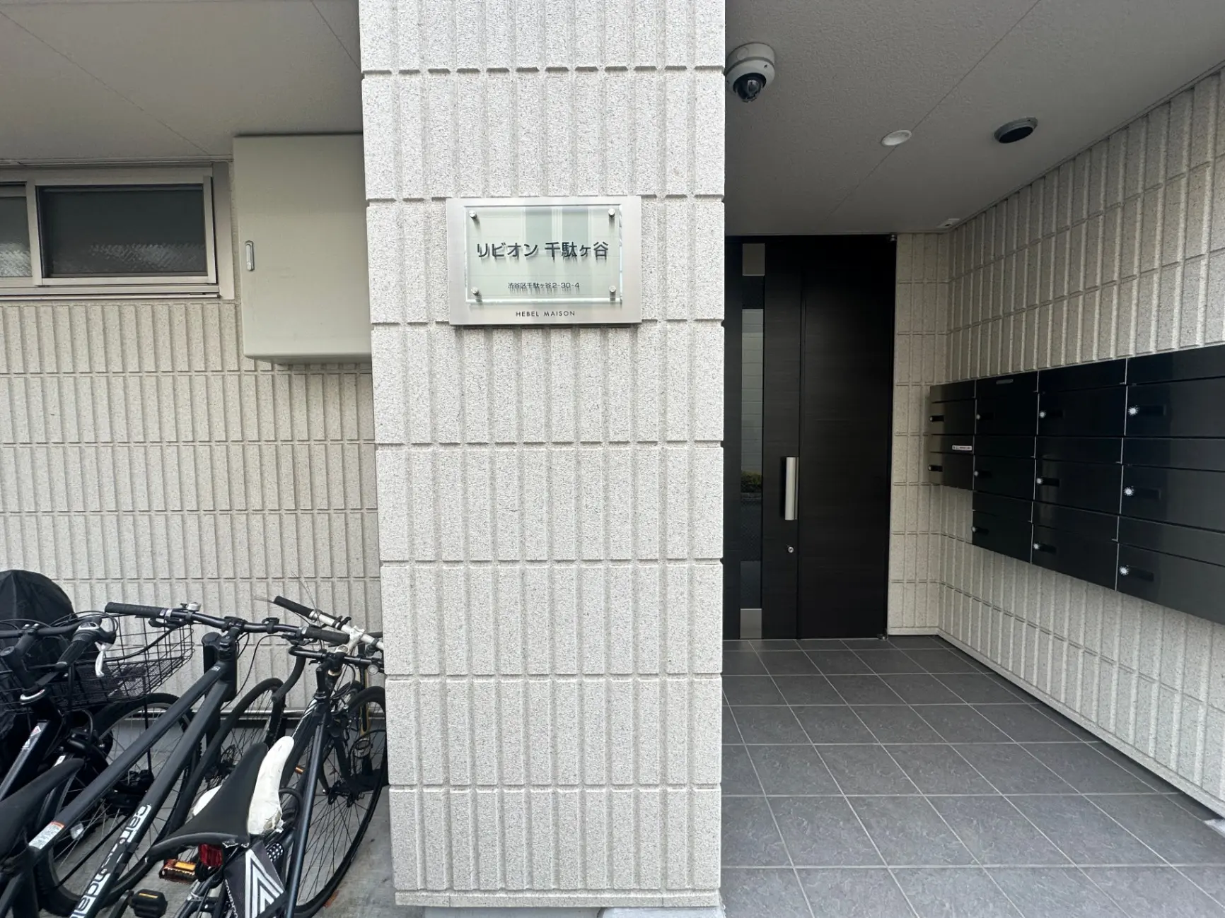 モダンなアパートの入り口、自転車が置かれた駐輪スペースと黒いポストが並ぶ壁