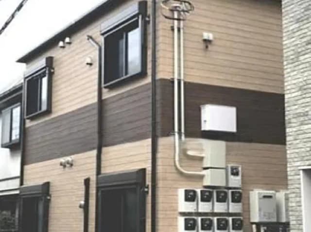 - モダンな外観の住宅、木材調とレンガ調の外壁、複数の窓と電気メーターが配置されたサイドビュー
