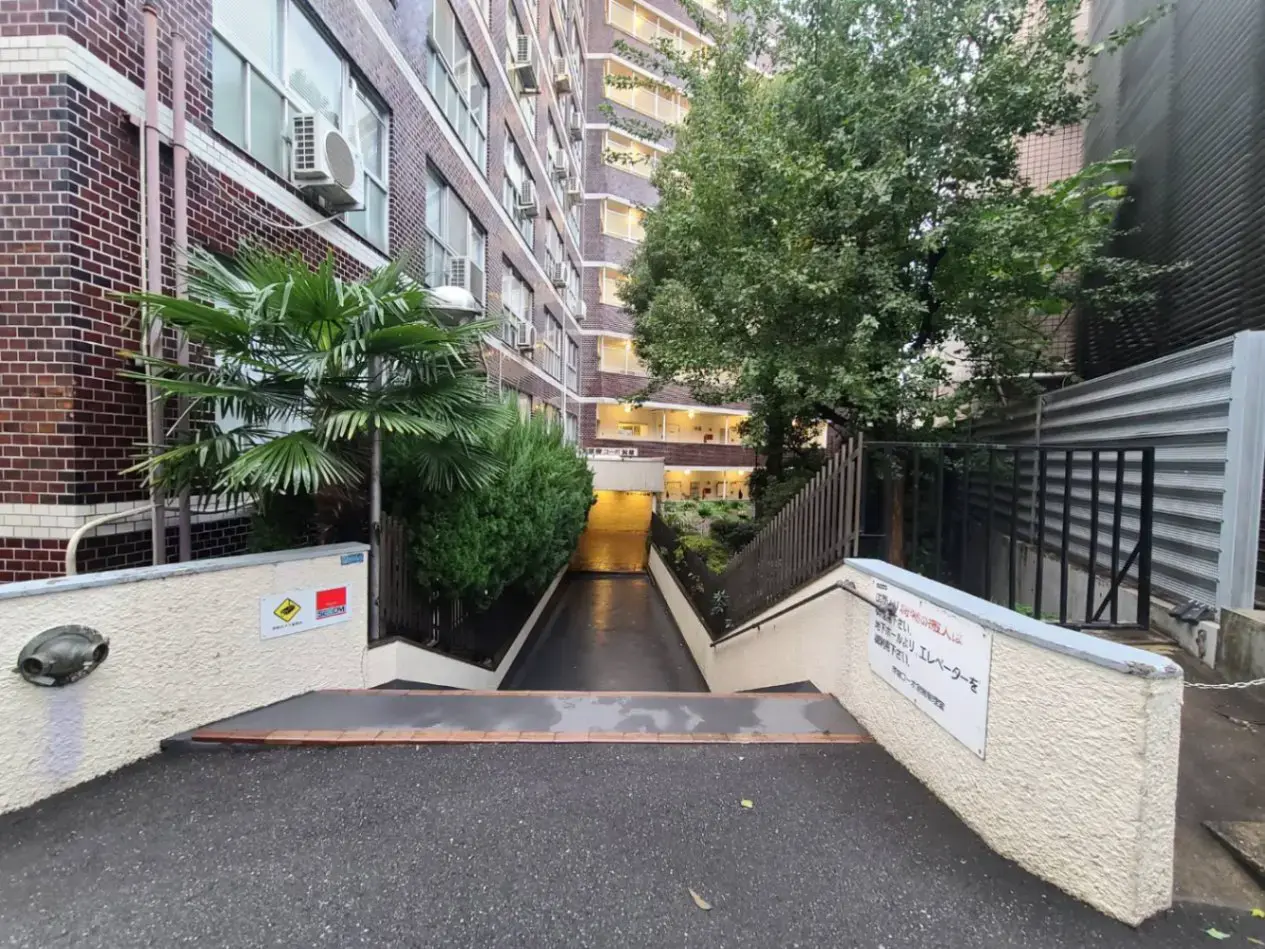 駐車場への坂道入り口と緑豊かな植栽がある建物の通路