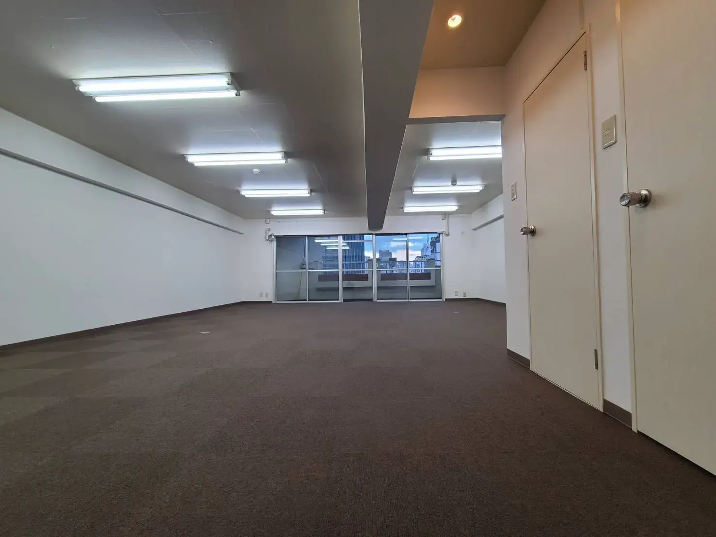 広々としたオフィススペース、フラットなカーペットの床、多数の蛍光灯が設置された天井