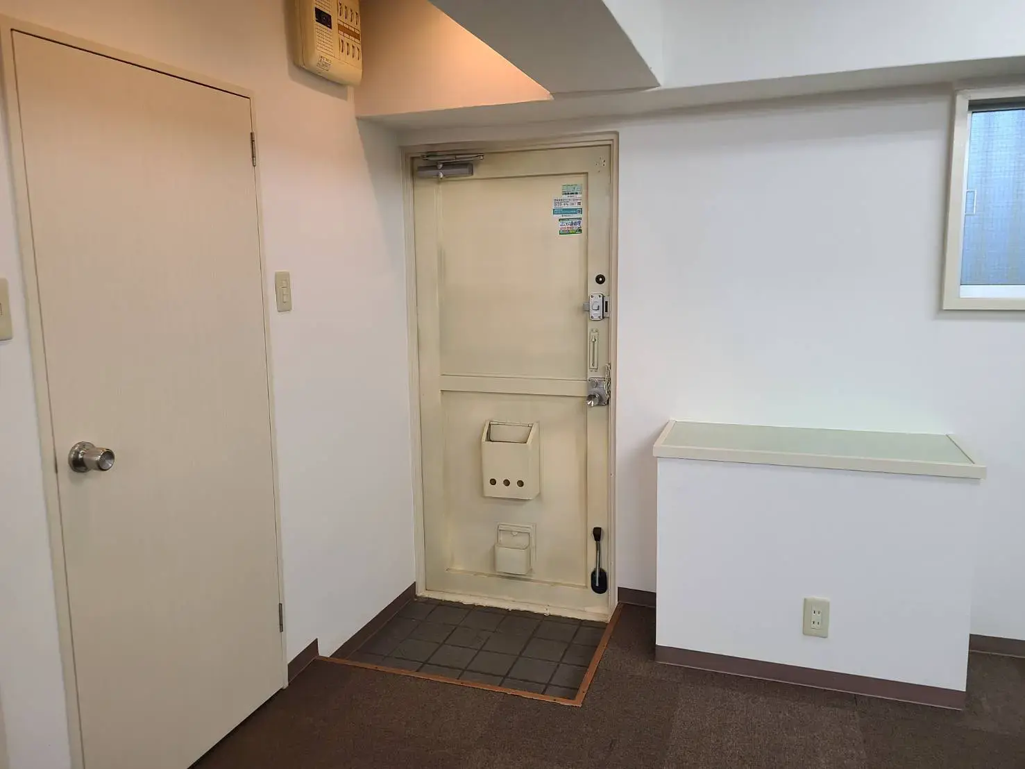 シンプルなデザインの玄関、白い壁と茶色のドアマット