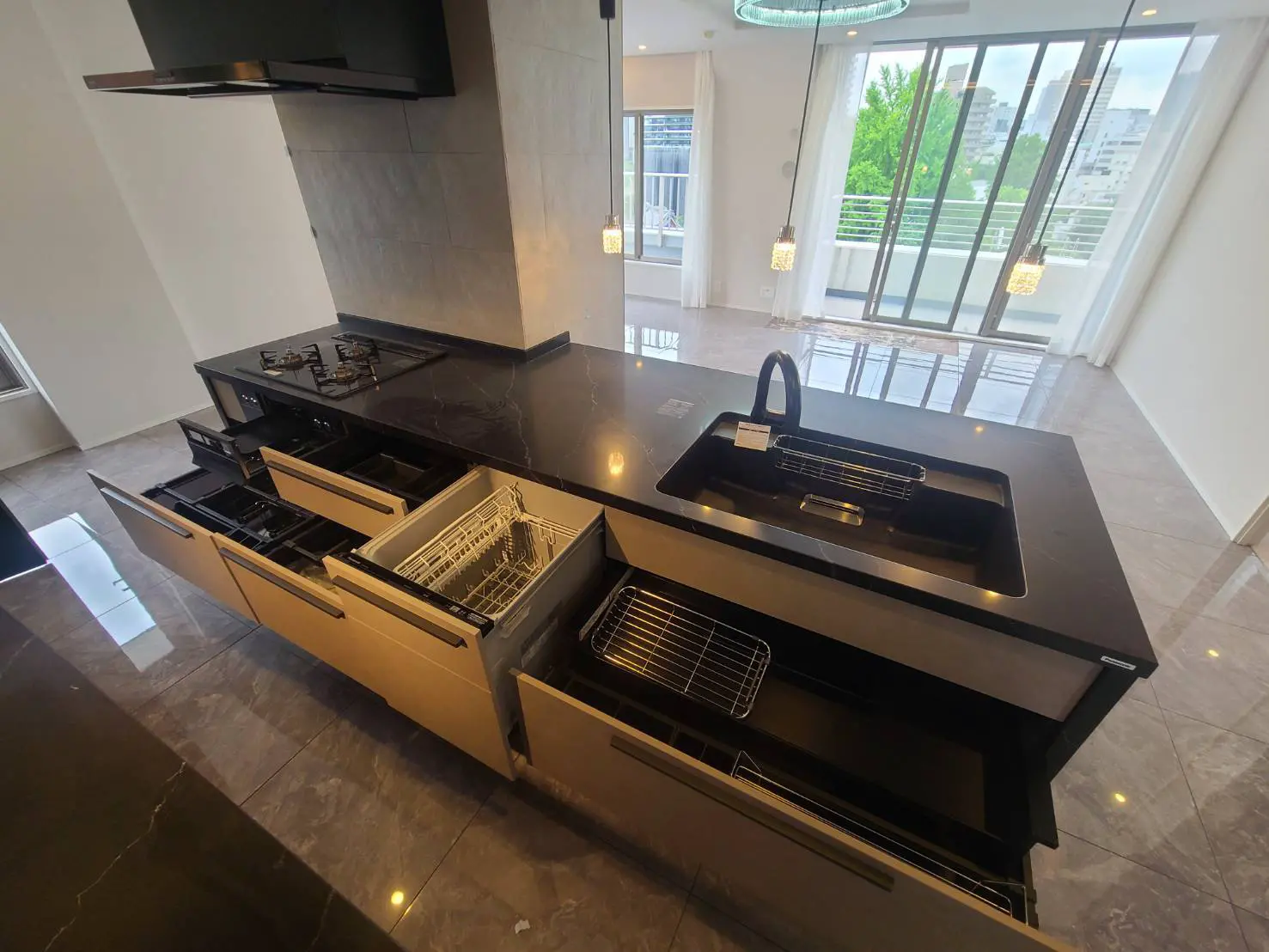 - モダンなキッチンのアイランドカウンター、黒い大理石の天板、引き出しと食器洗い機のある収納、明るい自然光が差し込む空間