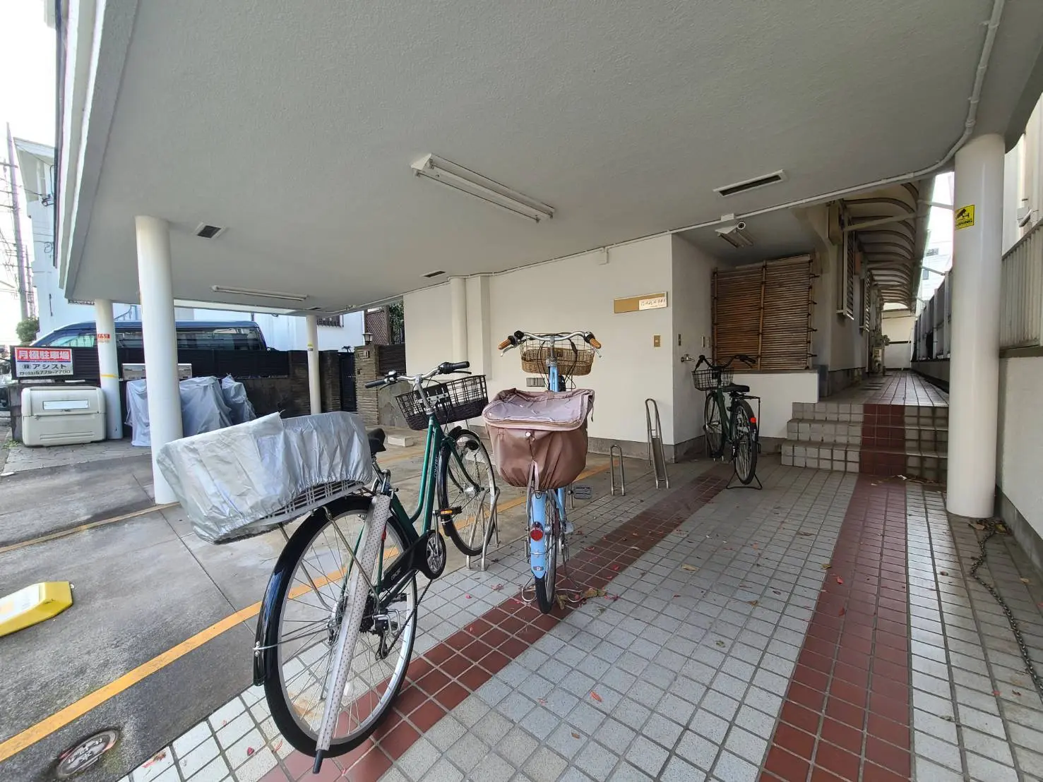 日本の住宅街にあるアパートの駐輪場、自転車が並ぶ屋根付きスペース、タイル張りの床
