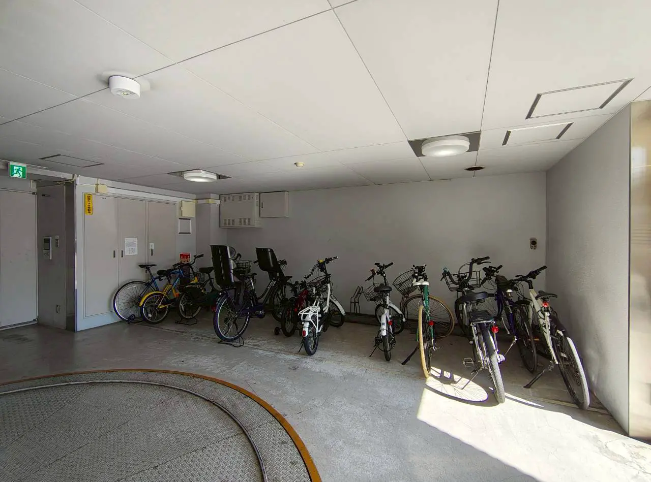 - 明るい照明の下に並んだ自転車がある駐輪場、壁はシンプルな白色で、空間に広がりが感じられるインテリア
