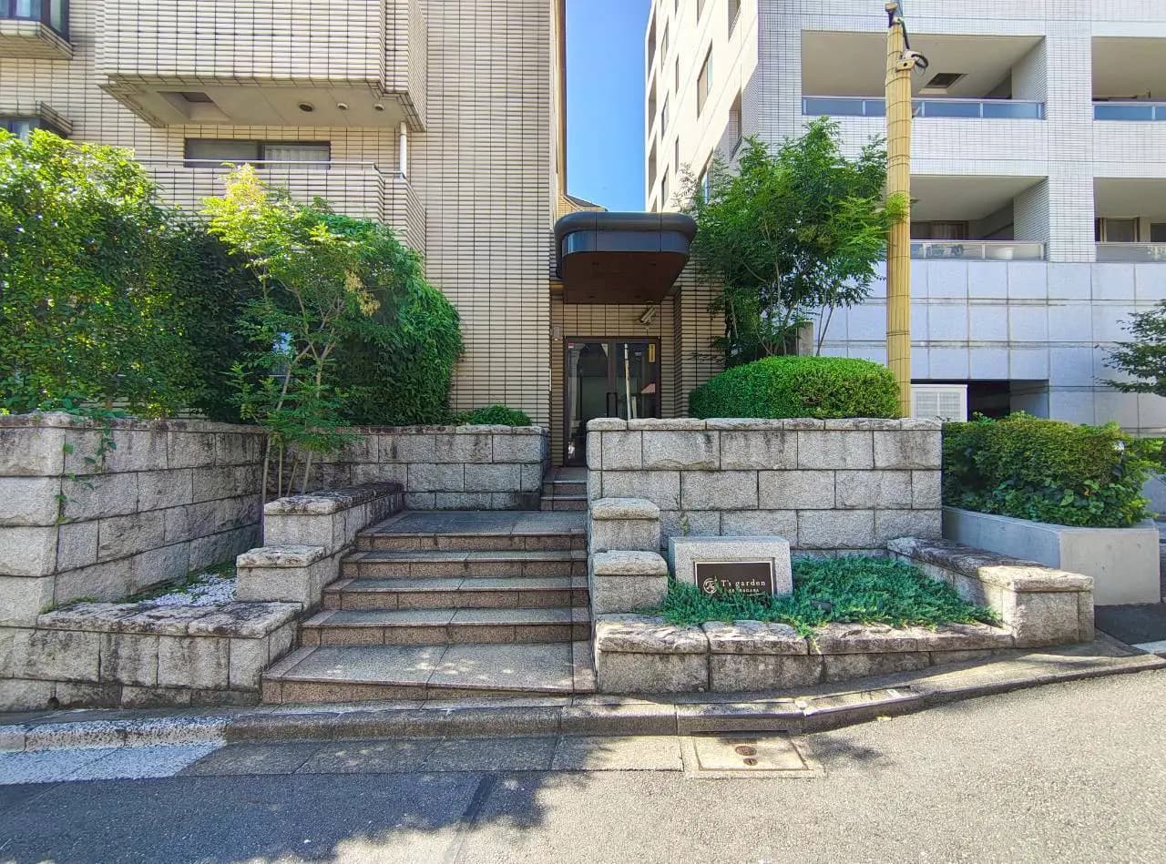 - 緑豊かなエントランスアプローチ、石造りの階段とシンプルな外観のマンション入り口、周囲には植栽が施された景観